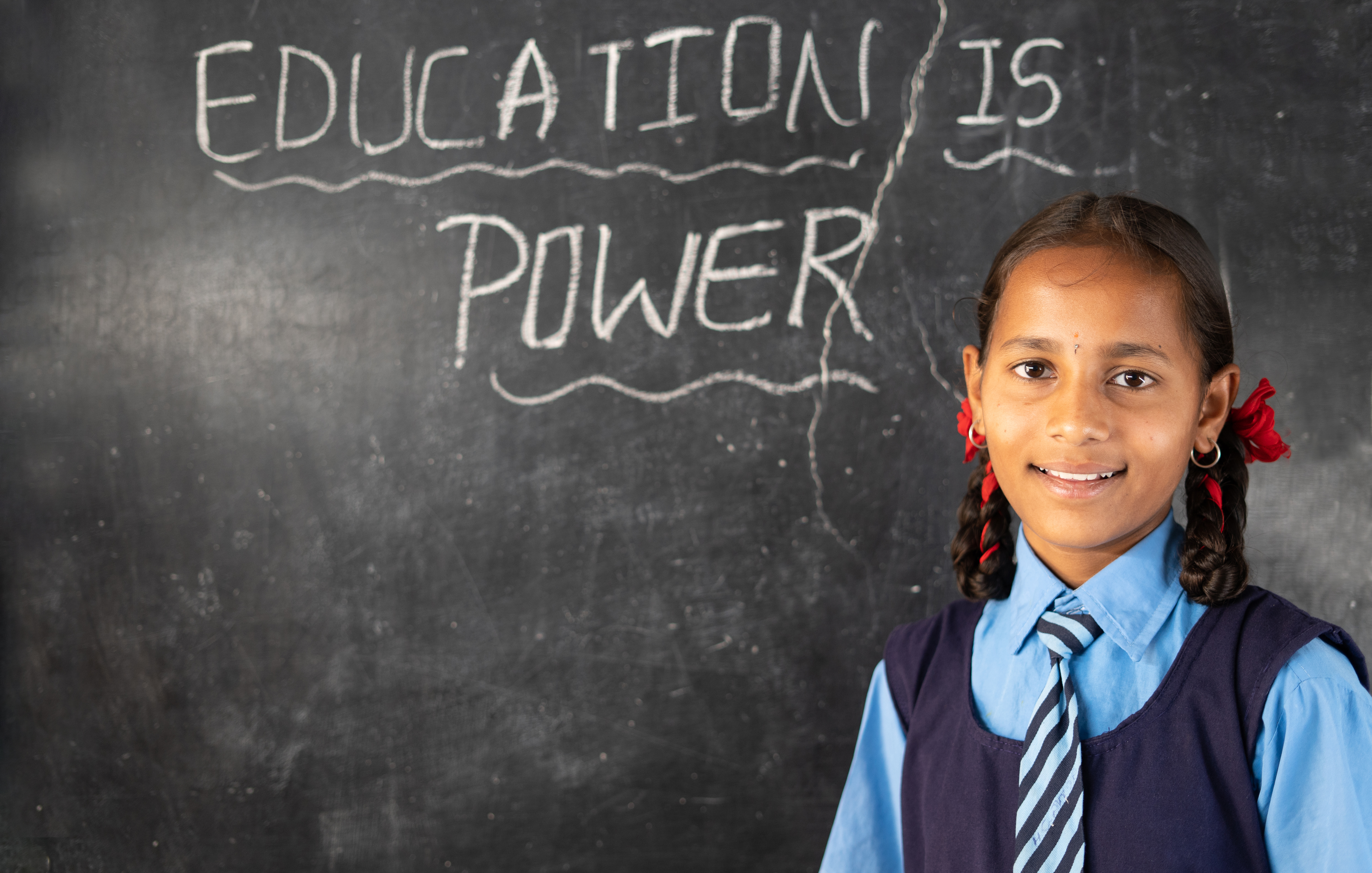 Schoolgirl in Maharashtra in front of a blackboard reading Education is Power